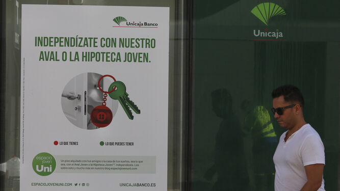 Un hombre pasa junto a una oficina de Unicaja Banco con un anuncio de una hipoteca.