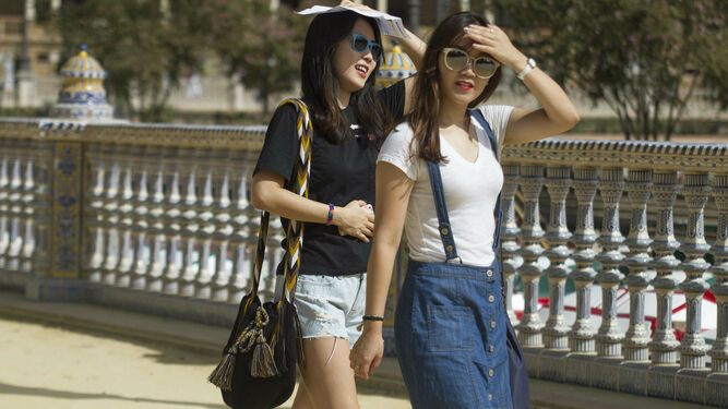 Dos jóvenes turistas asiáticas se cubren del sol en la Plaza de España ante las altas temperaturas de estos días en Sevilla.