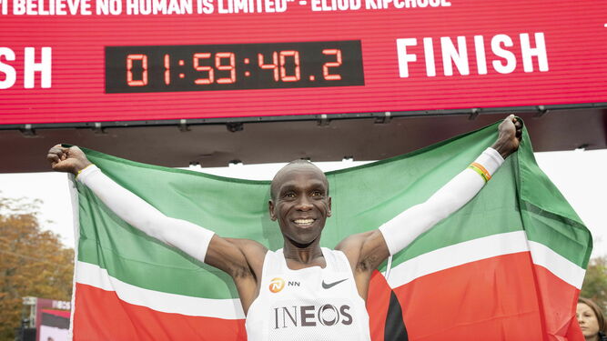 El keniano Eliud Kipchoge posa con la bandera de su país. Detrás su récord