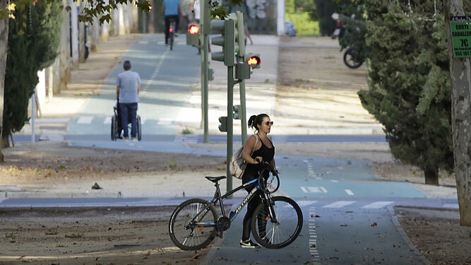 Una ciclista y una persona llevando a otra en una silla de ruedas por el carril bici de Los Bermejales.