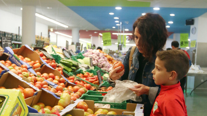 Una mujer selecciona unos tomates del estante de verdura de un supermercado.