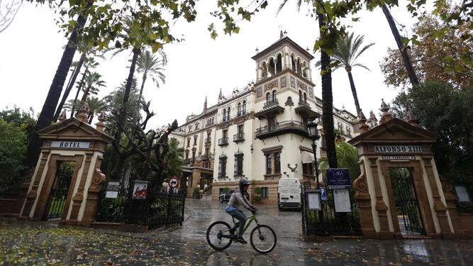 Un ciclista pasa frente al Hotel Alfonso XIII con la calzada cubierta de hojas de los árboles.