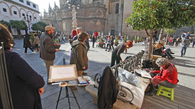 Varios turistas curiosean la obra de un pintor que retrata la Catedral de Sevilla.