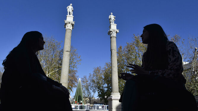 Dos chicas están sentadas en la Alameda de Hércules ante las emblemáticas columnas.