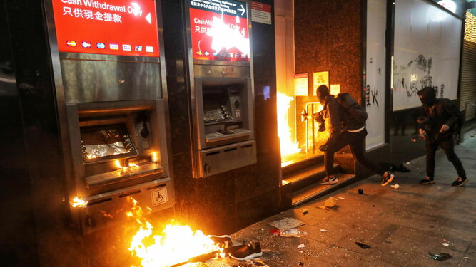 Dos manifestantes contra el Gobierno prenden fuego ayer a una sucursal bancaria en Hong Kong.