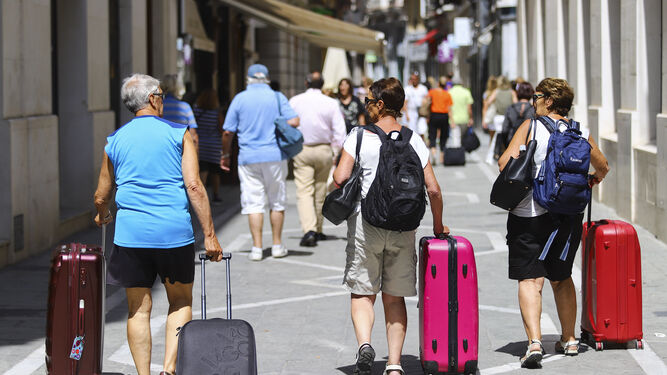Un grupo de turistas pasea con sus maletas por una calle de Málaga.