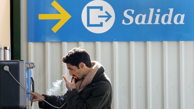 Un fumador habla por un teléfono público mientras sujeta un cigarrillo.