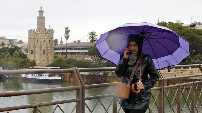 Una viandante se protege de la lluvia con un paraguas al pasar por el puente de San Telmo.