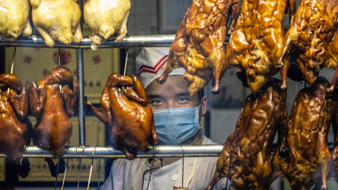 Un cocinero protegido con una máscara vende carne en un establecimiento de Guangzhou.