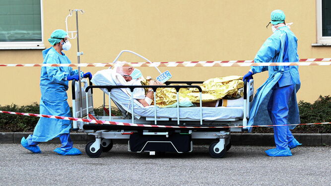 Dos trabajadores sanitarios trasladan aun afectado por coronavirus en el hospital italiano de Brescia.
