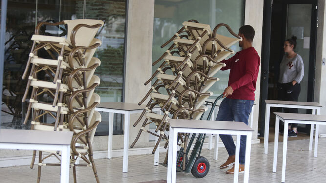 Un trabajador recoge las sillas de una terraza tras el decreto que obliga a cerrar estos establecimientos.