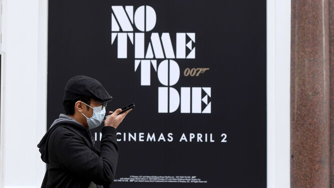 Un ciudadano con mascarilla, en Londres, ante un cartel con la antigua fecha de estreno de 'No Time To Die'.