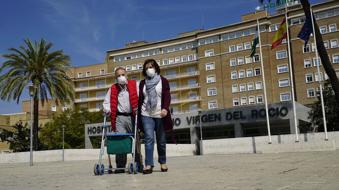 Un hombre y una mujer abandonan el Hospital Virgen del Rocío ataviados con mascarillas.