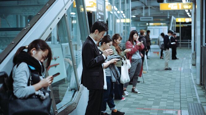 Japoneses en una estación de tren, con sus móviles en la mano.