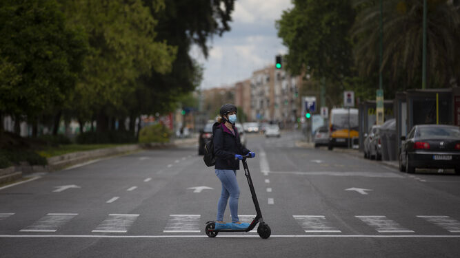 Una mujer cruza en patinete una solitaria avenida de de la ciudad.