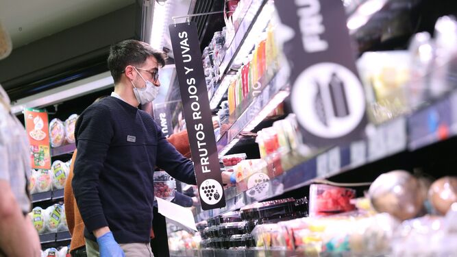 Un joven hacen la compra con mascarilla  y guantes en un supermercado.