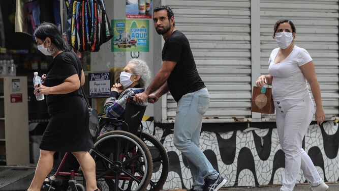 Un hombre conduce la silla de ruedas de una anciana con mascarilla.