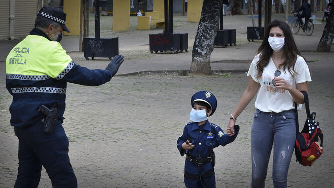 Un agente saluda a un niño vestido con el uniforme policial tras regalarle una mascarilla.