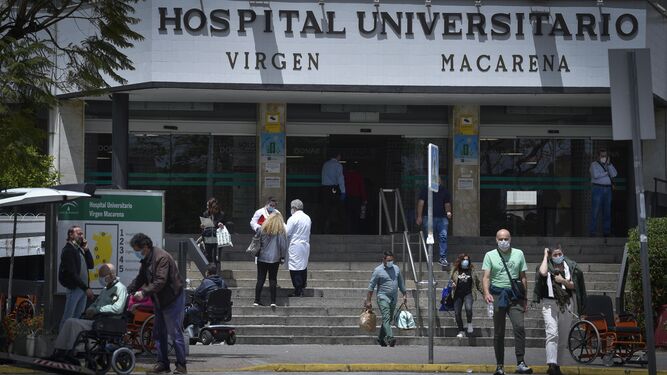 Varias personas y sanitarios coinciden en la puerta principal del Hospital Virgen Macarena.