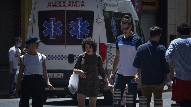 Varias personas caminan por la calle con una ambulancia de fondo.
