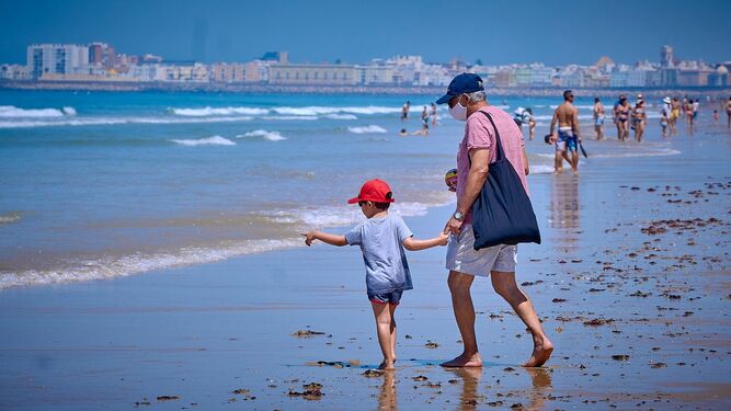 Varias personas pasean por la orilla de la playa de la Victoria, en Cádiz.