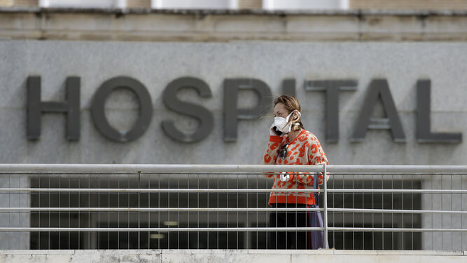 Una mujer con mascarilla delante en la entrada de un hospital.