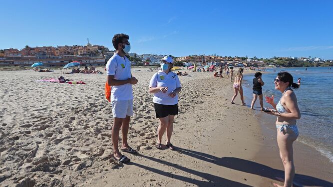 Dos auxiliares dialogan con una mujer en la orilla de la playa de Getares, este lunes.
