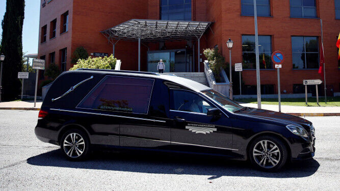 Un conductor protegido con una mascarilla espera en el interior de un vehículo de los servicios funerarios.