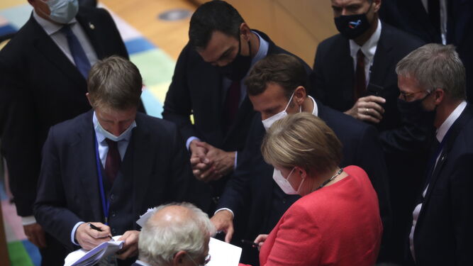 Angela Merlel, Enmanuel Macron, Pedro Sánchez y otros líderes, todos con mascarilla, ven la propuesta de Michel antes de iniciar la negociación.