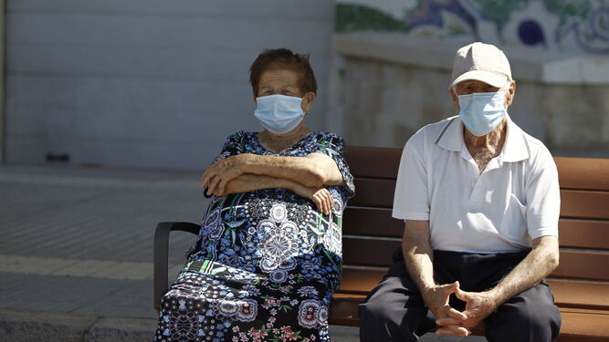 Dos ancianos descansan en un banco protegidos por mascarillas.