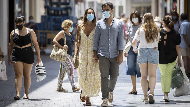 Gente con mascarilla paseando por un soleado centro de Sevilla.
