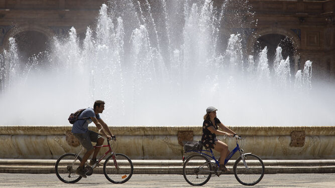 Dos personas en bicicleta pasan por la fuente de la Plaza de España.