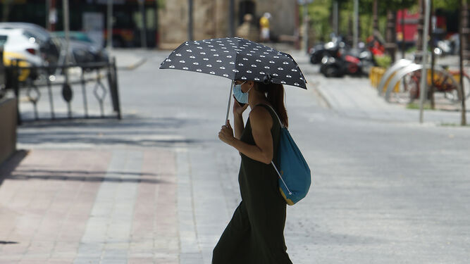 Una joven pasea por Sevilla con mascarilla y un paraguas para protegerse del sol