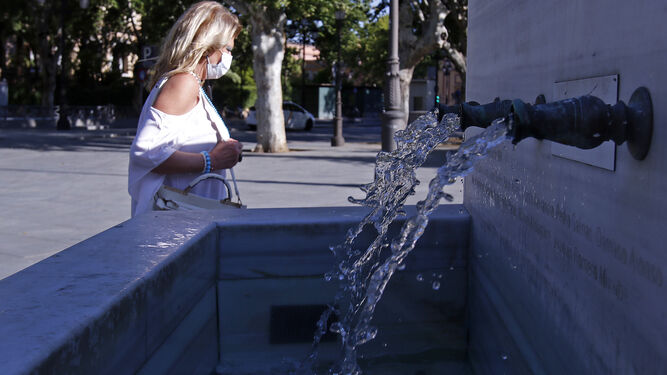 Una mujer pasa ante una fuente en Sevilla.