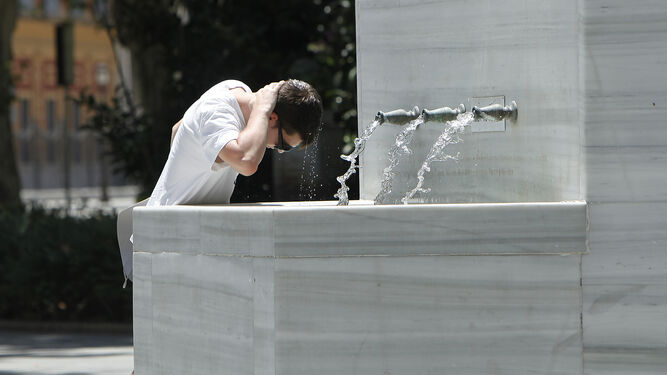 Un joven se refresca en una fuente de la ciudad.