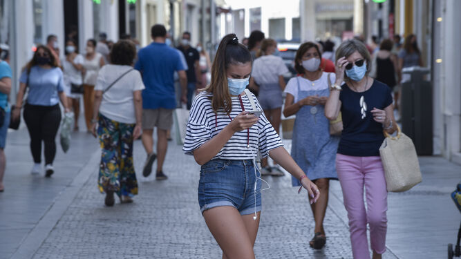 Una chica joven mira el móvil mientras camina por una abarrotada calle del centro de Sevilla.