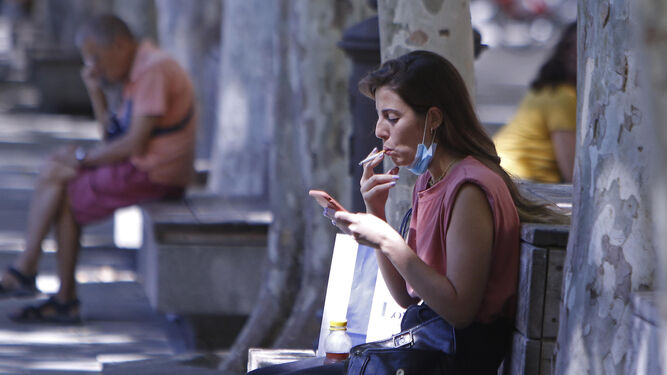 Una mujer fuma un cigarillo mientras mira el móvil