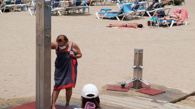 Una mujer con mascarilla se lava los pies en una ducha en Canarias.