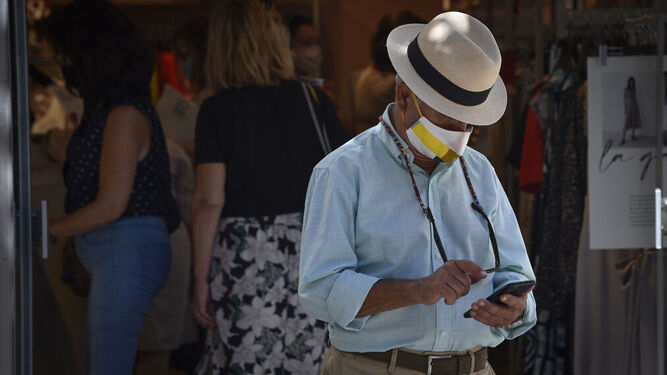 Un hombre, con mascarilla, mira su móvil en la calle.