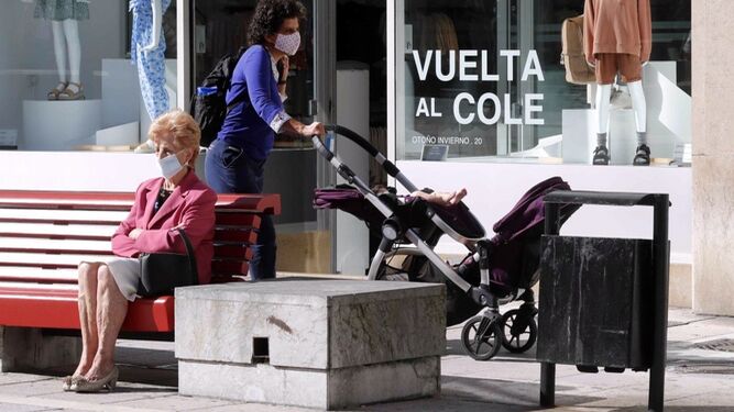 Una mujer pasa con su bebé junto a un comercio en Oviedo.