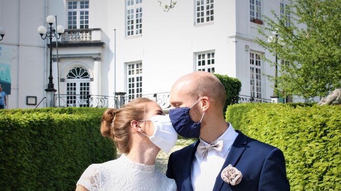 Una pareja de recién casados celebra el momento besándose con mascarillas.