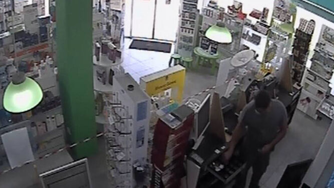 El atracador robando el dinero de la caja de una farmacia.