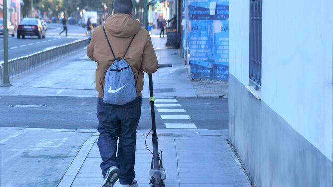 Un usuario camina con su patinete cerca del centro de la ciudad.