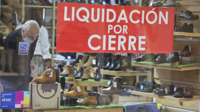 Un hombre mira los artículos de una zapatería de Málaga que anuncia el cierre.
