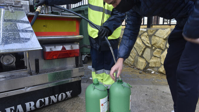 Un operario de la empresa del Plan Écija llena garrafas de agua con un camión cisterna.