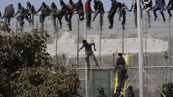 Inmigrantesencaramados a la valla de Melilla y agentes abajo.