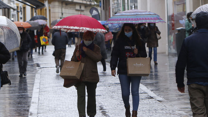 Varias personas caminan por el centro de la ciudad en una mañana lluviosa.