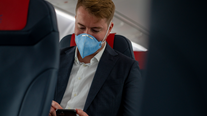 Un viajero con su mascarilla en el interior de un avión