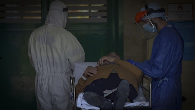 Dos sanitarios junto a un paciente en el momento de su hospitalización en un centro sevillano.