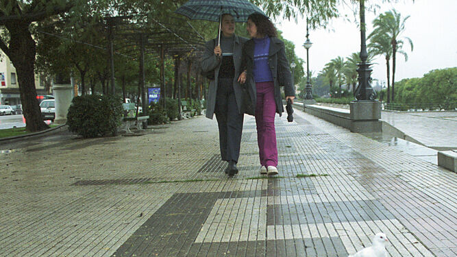 Dos chicas pasean junto al río Guadalquivir bajo un paraguas.